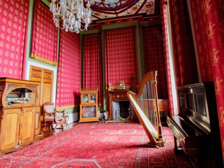 A crimson bedroom with a harp, four-poster and chandelier, Allerton Castle