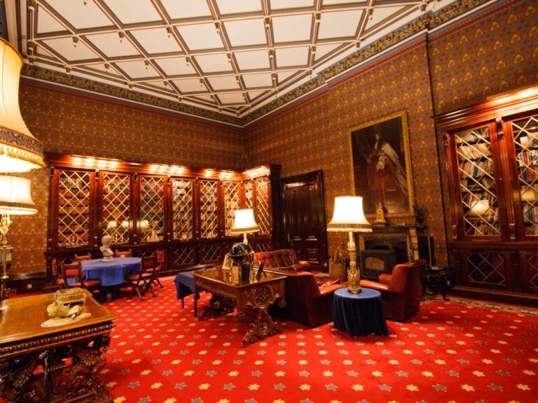 A panelled room with a coffered ceiling, portraits and a red carpet, Allerton Castle