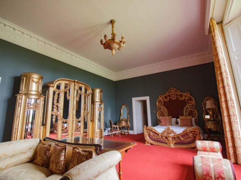A sage-green bedroom with an ornately carved bed and a chandelier, Allerton Castle