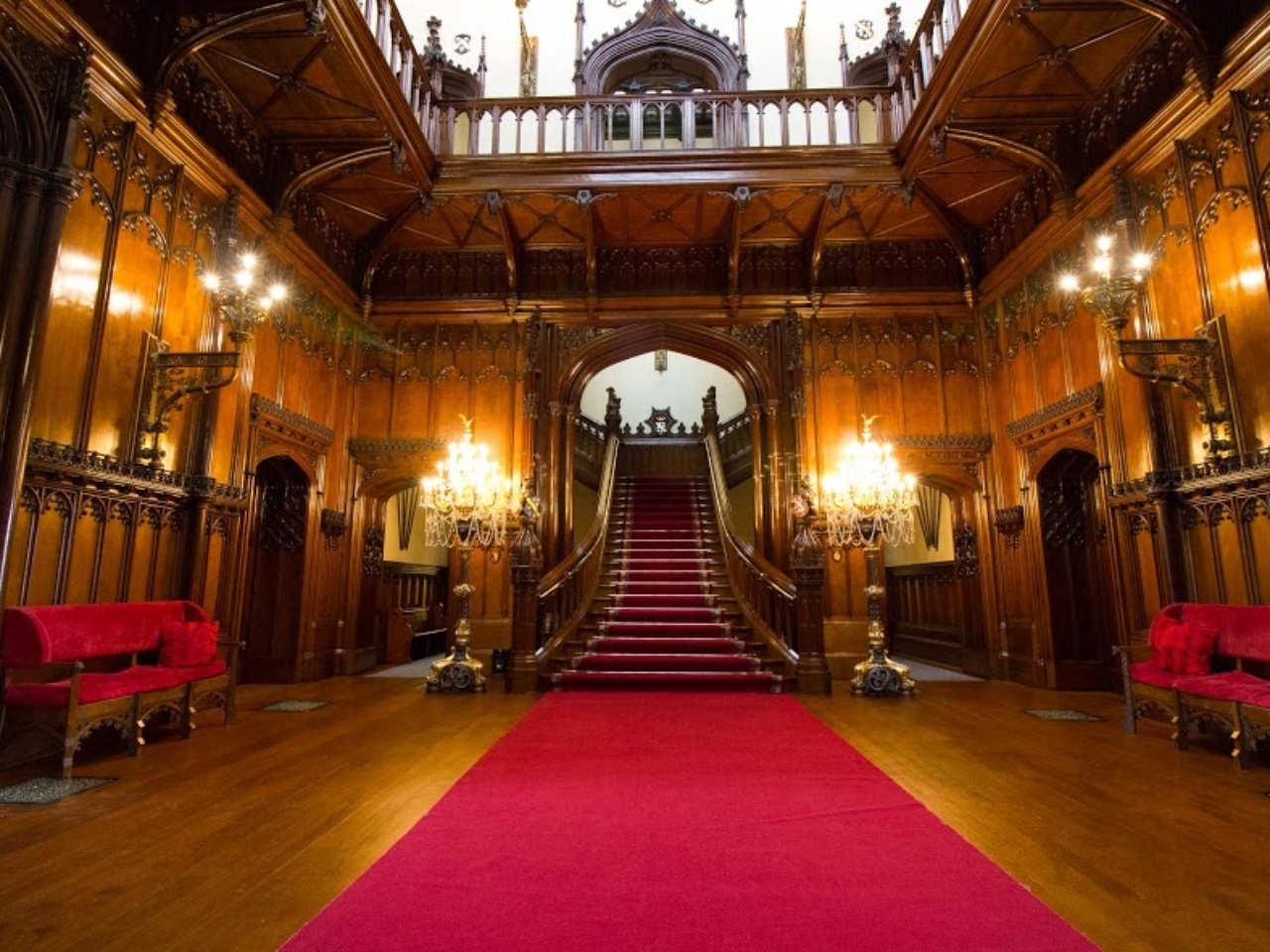 The Great Hall, its oak-panelled walls and grand red-carpeted staircase lit warm for the evening, Allerton Castle