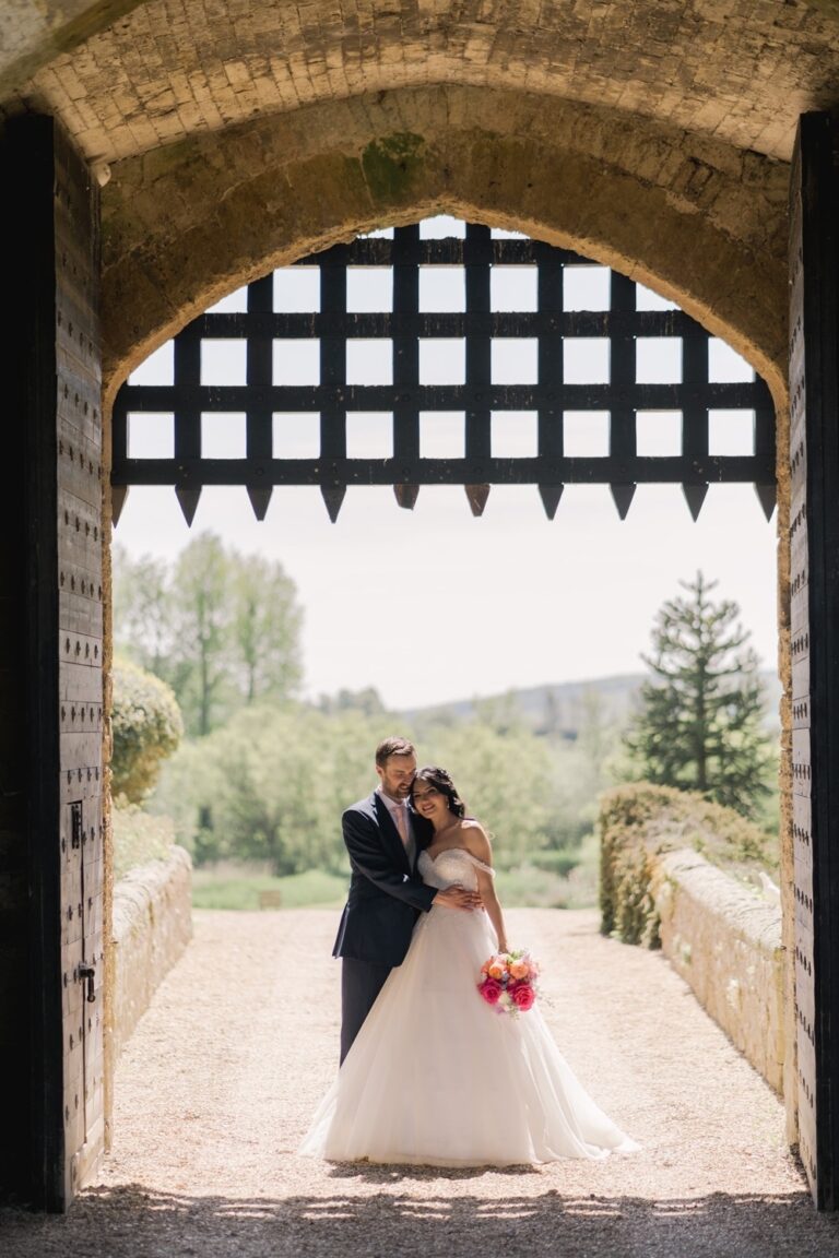 A couple embracing under the stone gatehouse arch, the South Downs beyond, Amberley Castle