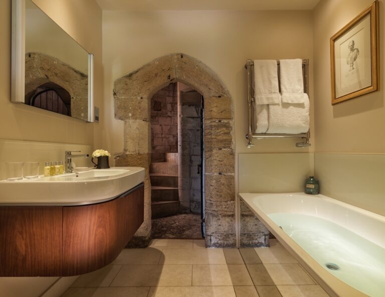 A bathroom built around a medieval stone archway, with a walnut vanity and tub, Amberley Castle