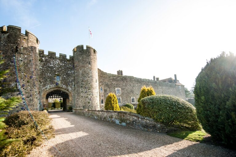Amberley Castle at golden hour, its twin drum towers and gatehouse rising above the gravel approach and clipped topiary, Amberley Castle