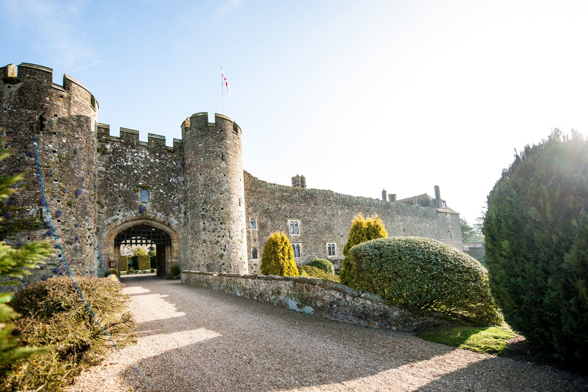 Amberley Castle at golden hour, its twin drum towers and gatehouse rising above the gravel approach and clipped topiary, Amberley Castle