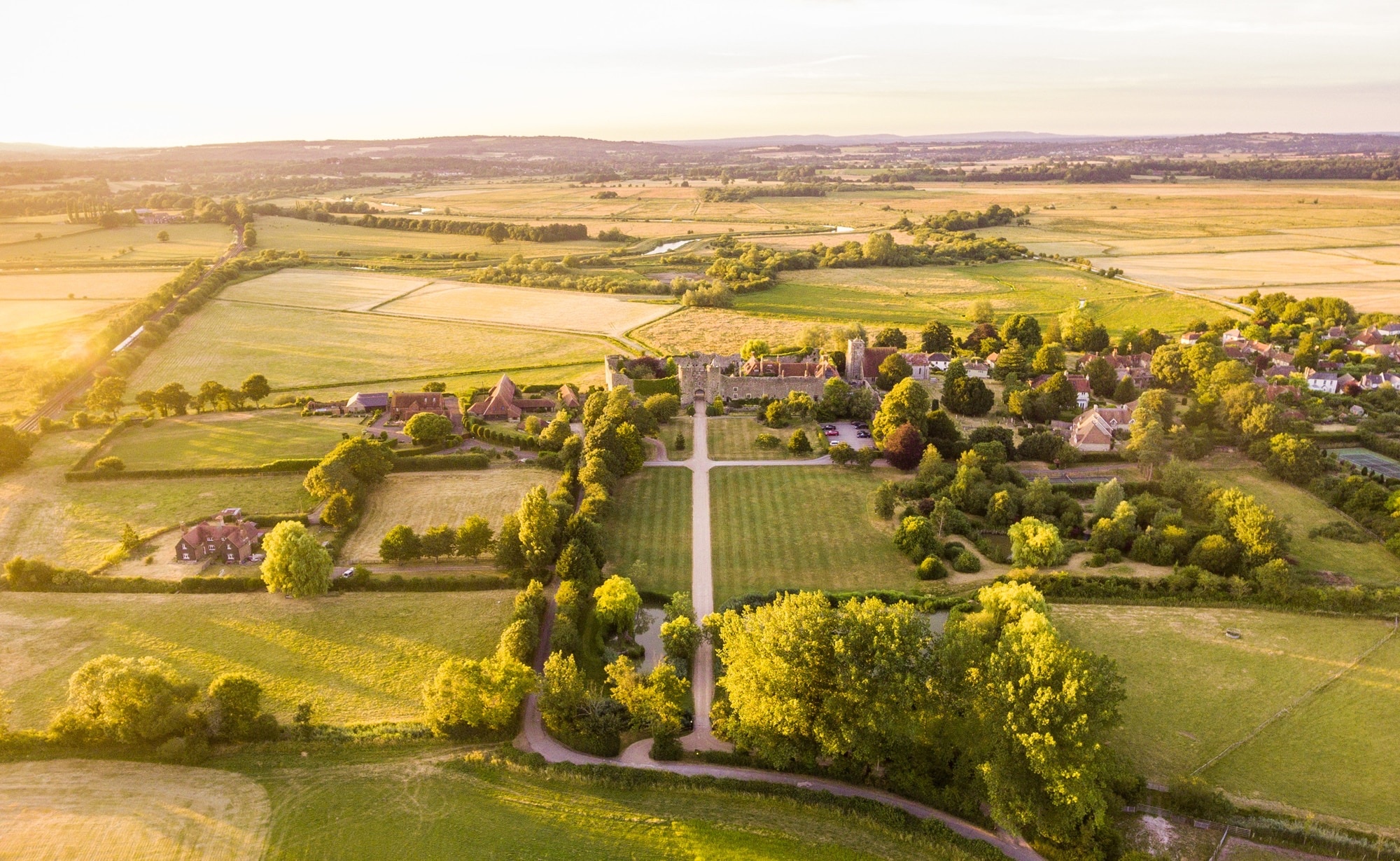 An aerial view of the castle and its walled gardens set in the rolling South Downs, lit by late afternoon sun, Amberley Castle