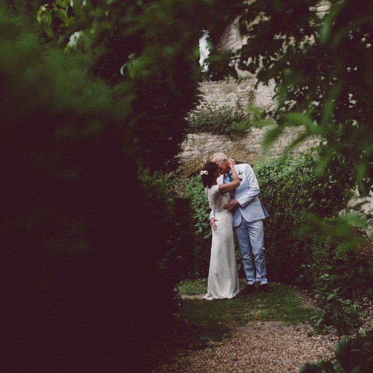 A newly married couple sharing a kiss on a garden path between high hedges, Amberley Castle