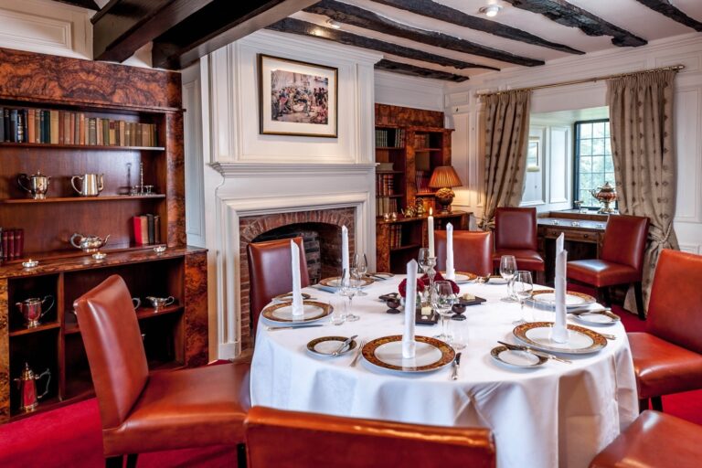 A panelled dining room lined with books, a round table laid for dinner by the fire, Amberley Castle