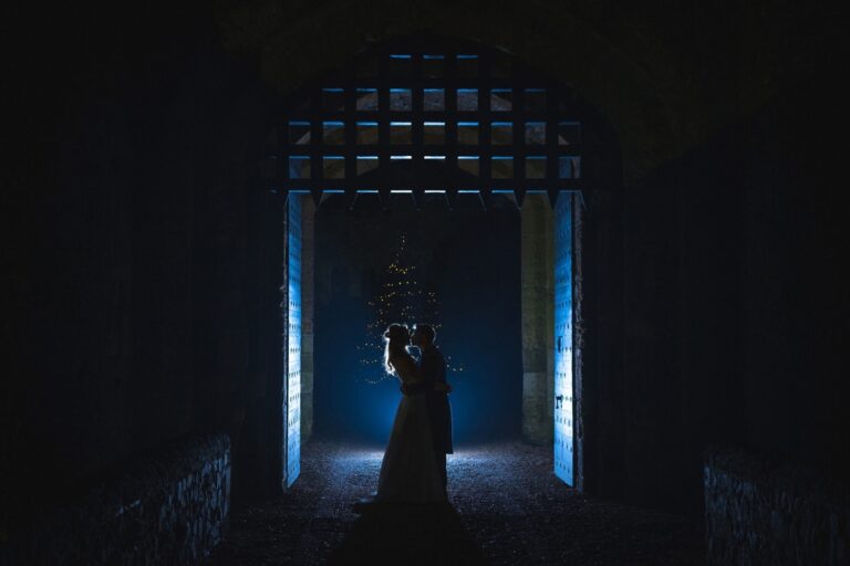 A couple silhouetted in the portcullis gateway at night, framed by warm light, Amberley Castle