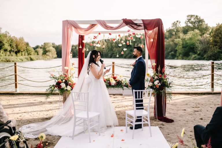 Ceremony under a draped floral arch on a riverside beach, Lake Garda, Angela Salzano