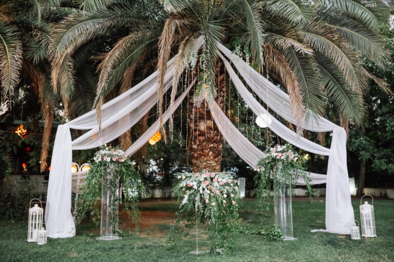 White drapes and flower arrangements set beneath palm trees, Angela Salzano