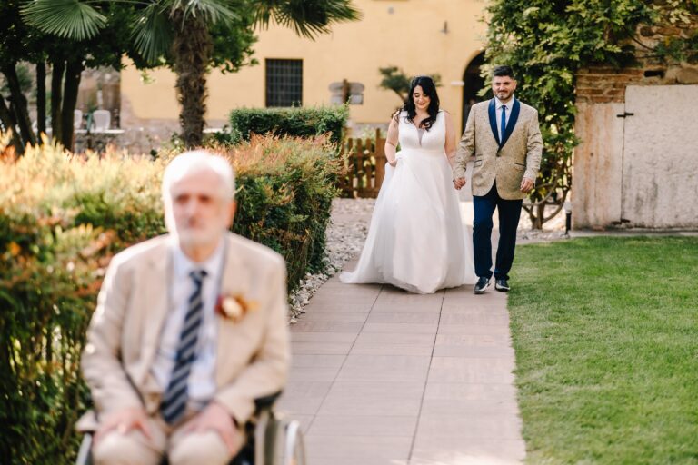 The couple walking along a garden path past a seated guest, Angela Salzano