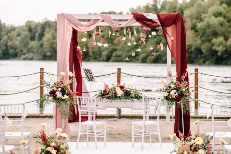 Floral arch with draped fabric and hanging blooms on the shore, Angela Salzano