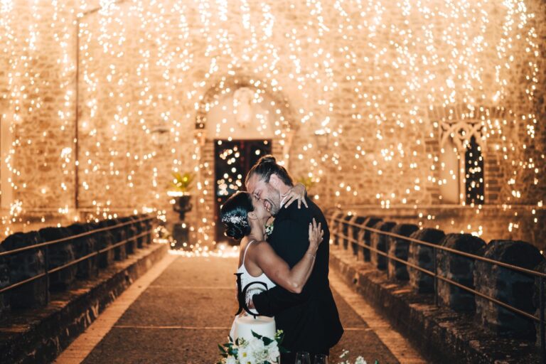 The kiss in front of a wall of fairy lights, the cake standing at their feet, Anita Galafate