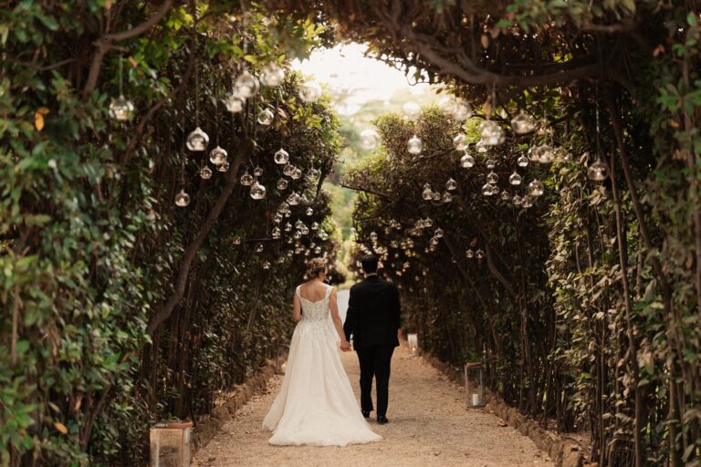 A pergola tunnel hung with glass globes, the couple walking away down the path, Anita Galafate