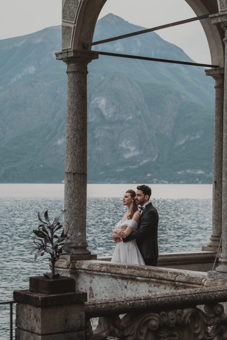 The couple under a lakeside loggia, the mountains rising across the water, Anita Galafate