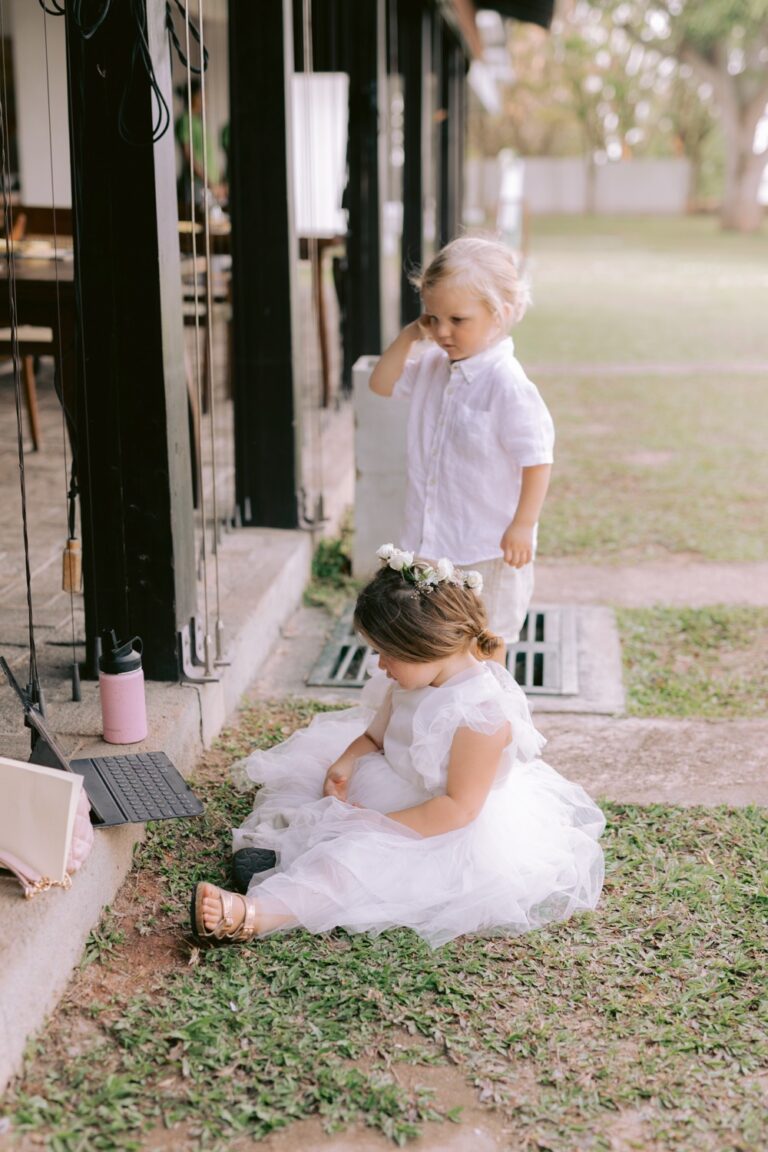 Two small children in white dresses and flower crowns on the grass outside a pavilion, Anywhera Events The Destination Wedding Planner in Sri Lanka