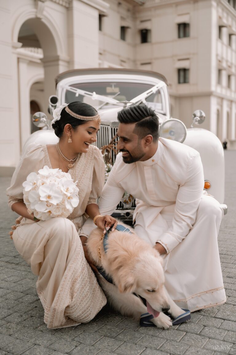 A couple in cream outfits crouched with a golden retriever beside a vintage wedding car, Anywhera Events The Destination Wedding Planner in Sri Lanka