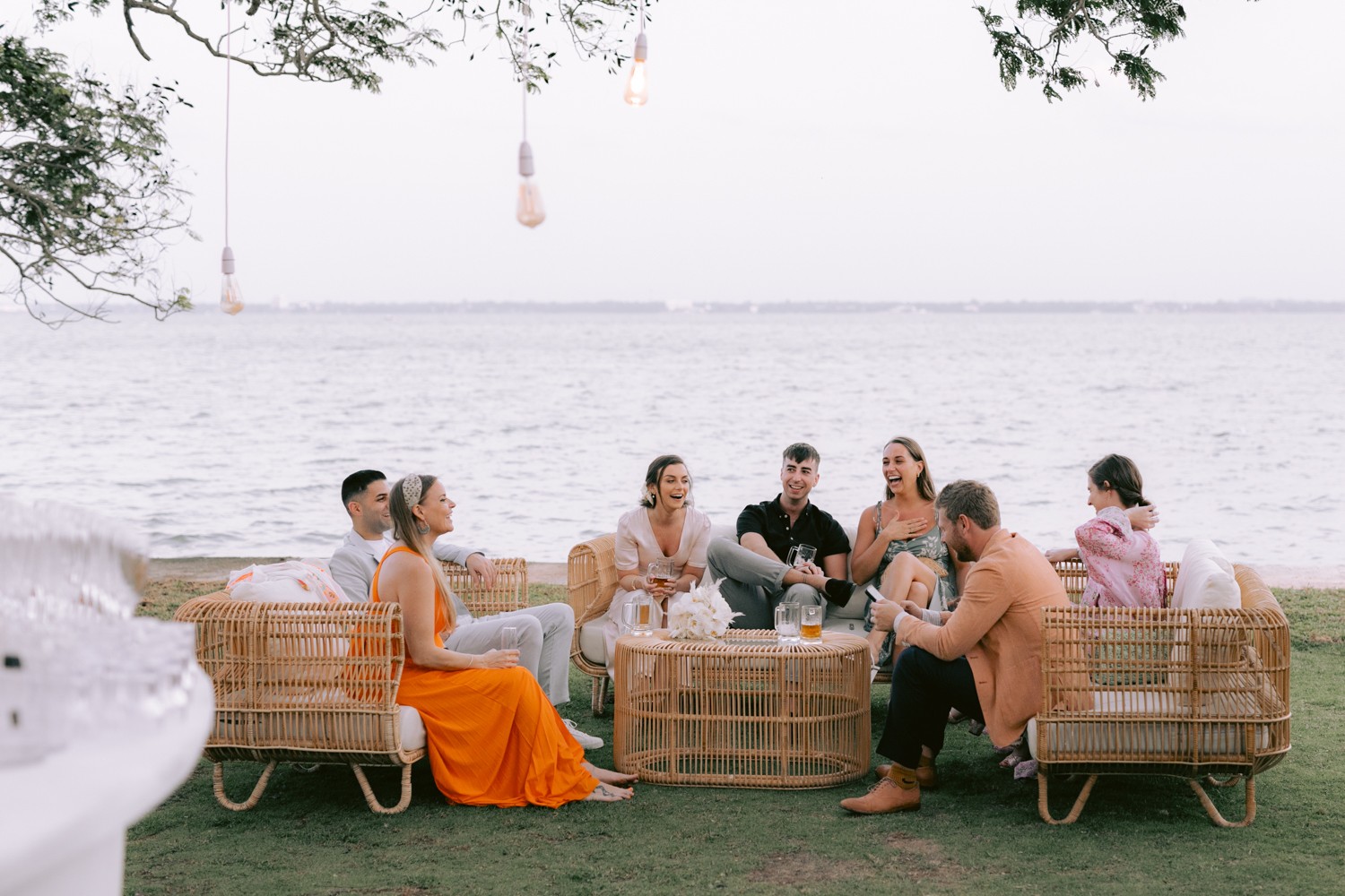 Guests seated on rattan sofas on the grass beside the water at dusk, Anywhera Events The Destination Wedding Planner in Sri Lanka