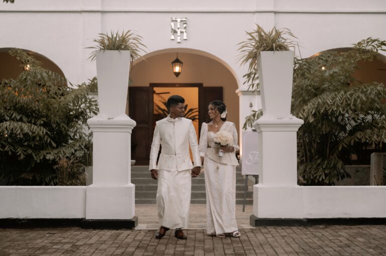A couple in white walking out of a whitewashed colonial-style arched entrance, Anywhera Events The Destination Wedding Planner in Sri Lanka