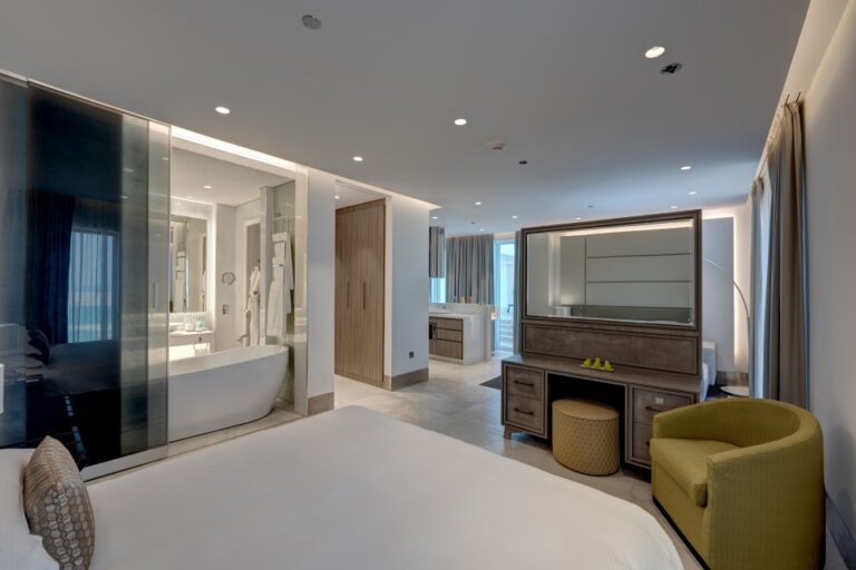 A suite bedroom with a dressing table and bathroom beyond, Arjaan by Rotana Dubai Media City