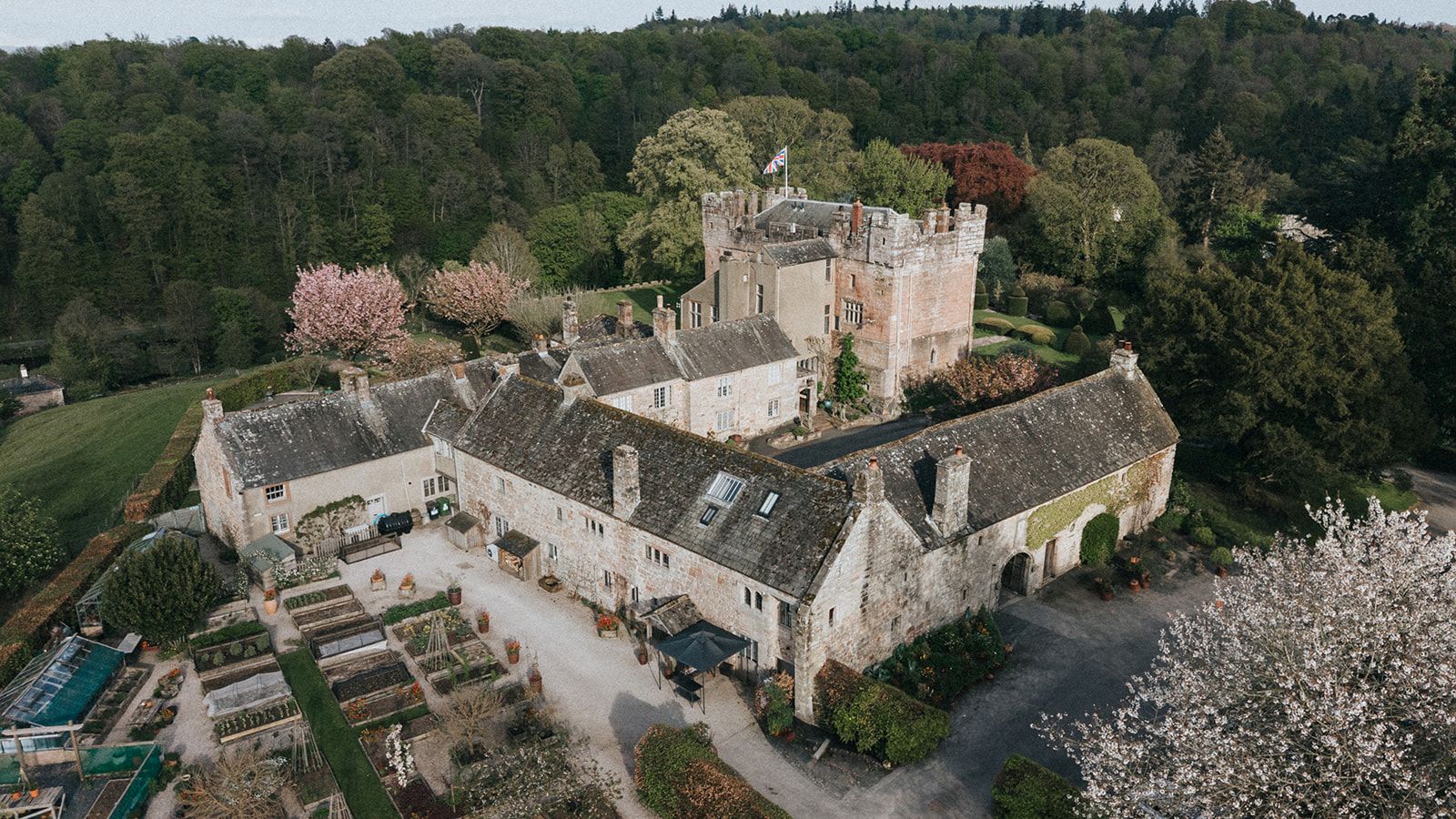 Aerial view of the pele tower, the courtyard wings and the kitchen garden beds in spring blossom, Askham Hall