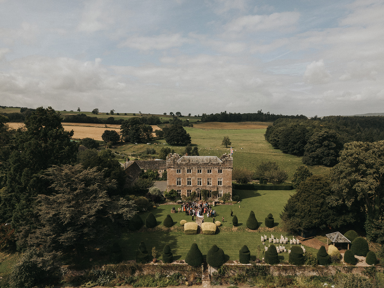 Aerial view over the topiary lawn to the hall, with ceremony chairs and the garden pavilion set out and farmland beyond, Askham Hall