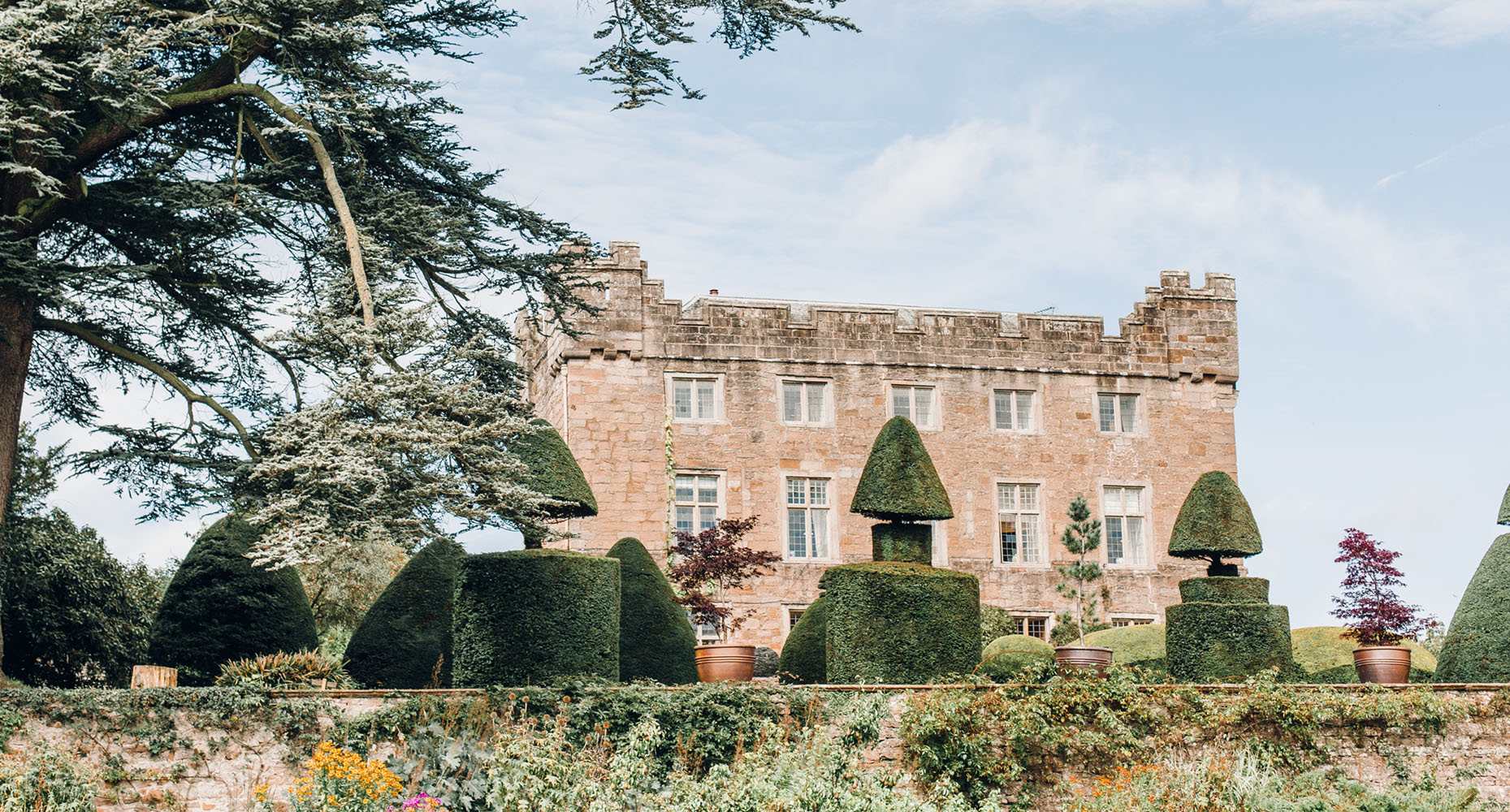 The castellated sandstone front of Askham Hall above the clipped yew topiary and planted terrace walls, Askham Hall