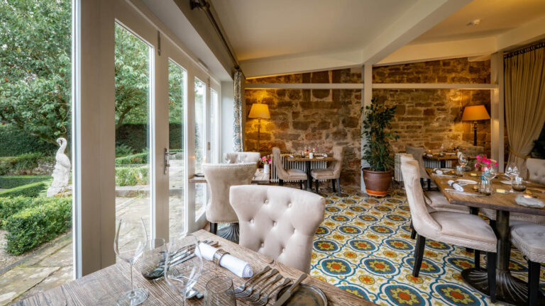 The dining room of Allium, with tiled floor, stone walls and doors onto the garden, Askham Hall