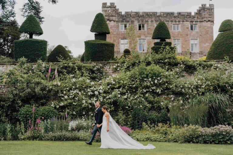 A couple walking the front lawn beneath the herbaceous border, with the hall and topiary above, Askham Hall