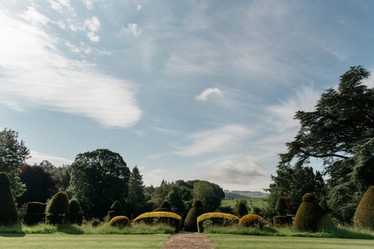 The topiary lawn and its brick path, looking out to the fells under a wide sky, Askham Hall