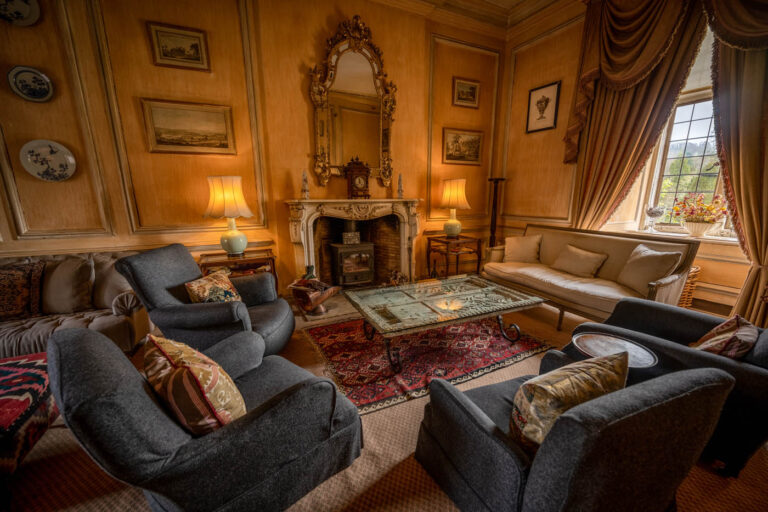 A panelled sitting room in the hall with a marble fireplace, gilt mirror and armchairs, Askham Hall