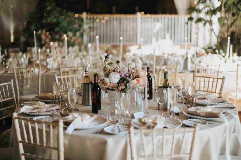 A round table in Bank Barn dressed with pale linen, taper candles and garden roses, Askham Hall