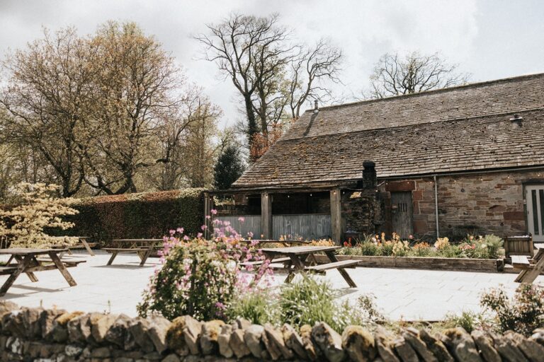The paved terrace outside Bank Barn, with picnic benches and spring planting, Askham Hall