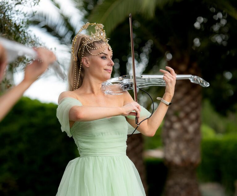 An electric violinist in a green gown playing outdoors for a ceremony, Aston Band