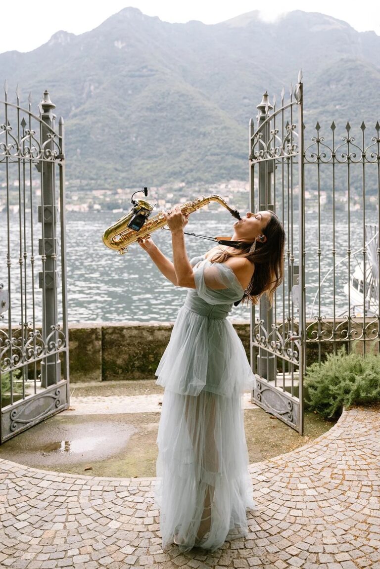 A saxophonist playing at an open wrought-iron gate above a mountain lake, Aston Band