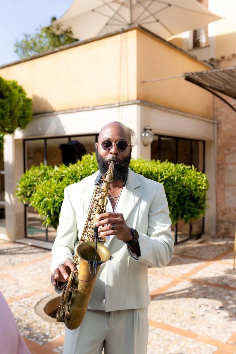 A saxophonist in a white suit playing in a sunlit courtyard, Aston Band