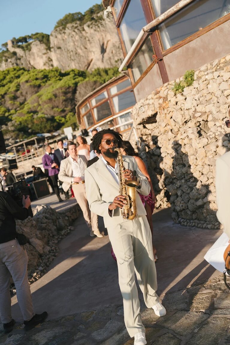 A saxophonist in a cream suit walking along a cliffside terrace, Aston Band