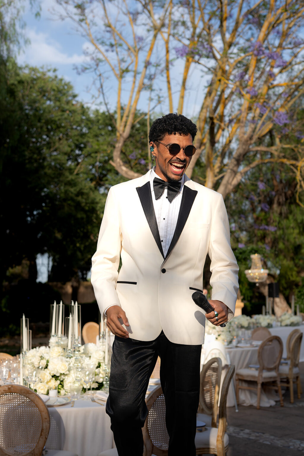 A singer in a white dinner jacket walking between the tables at a wedding dinner