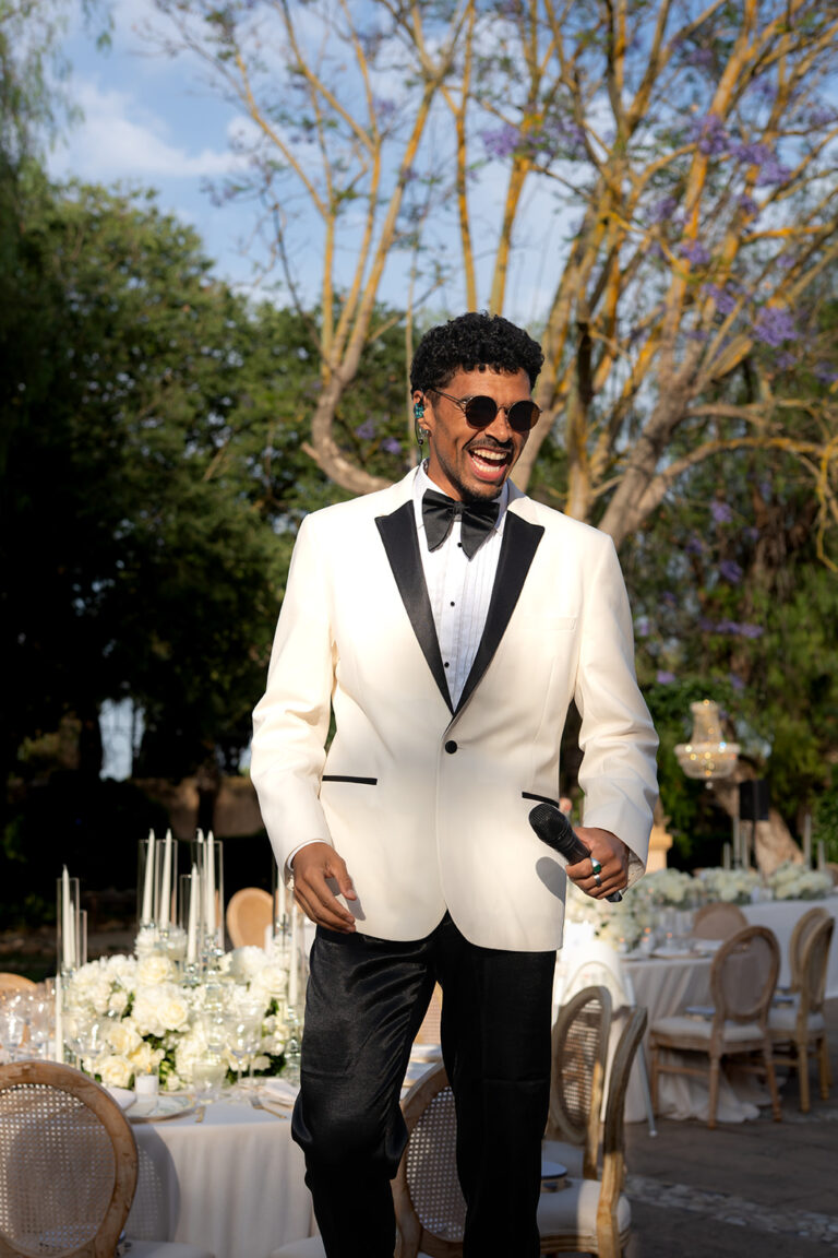 A singer in a white dinner jacket walking between the tables at a wedding dinner, Aston Band