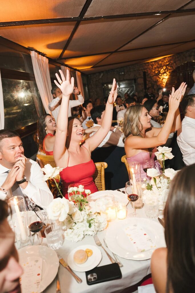 Guests with arms raised at a candlelit wedding dinner, Aston Band