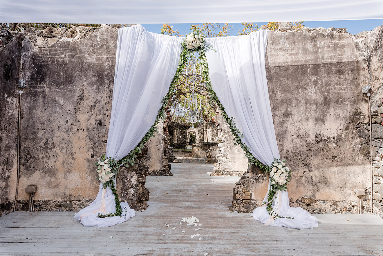 White drapes and green garland framing a ceremony arch in a ruined stone building, Awesome Caribbean Weddings