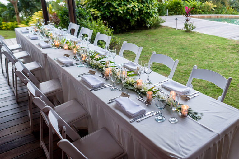Long table on a lawn dressed with a floral runner, napkins and white chairs, Awesome Caribbean Weddings