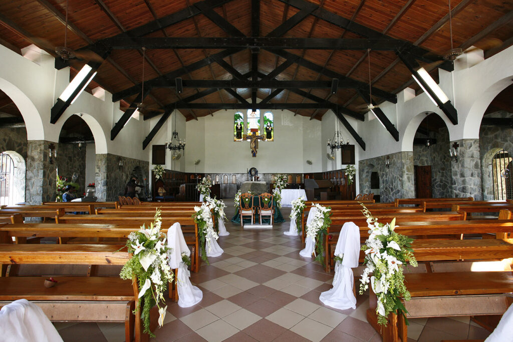 A chapel with wooden pews and white flowers at the front