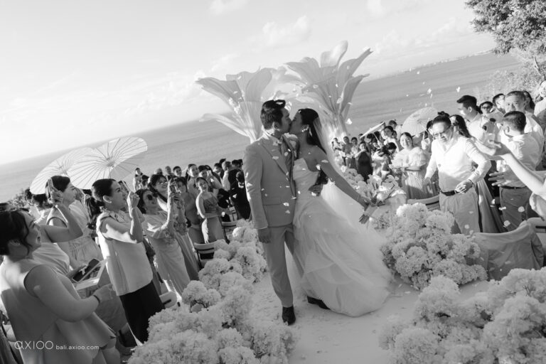 Black and white frame of a couple walking the aisle between guests above the sea, Bali, Axioo Bali