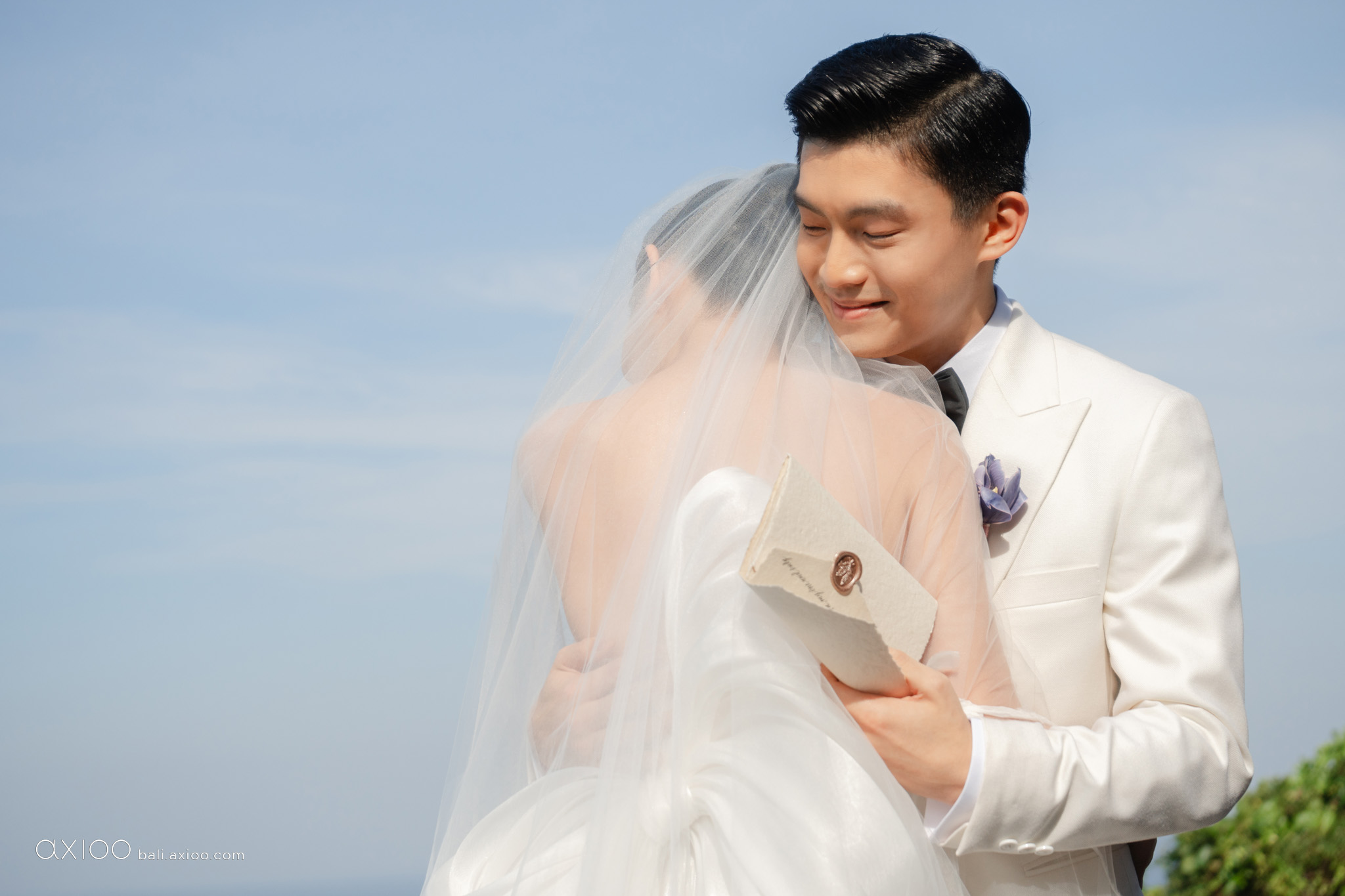 Bride and groom embracing under a veil against a clear blue sky, Bali, Axioo Bali