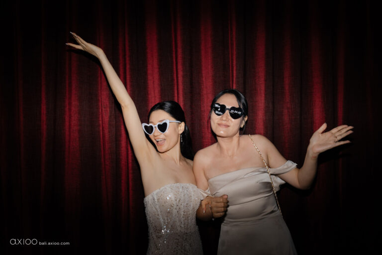Two guests posing with heart-shaped sunglasses against a red curtain, Bali, Axioo Bali