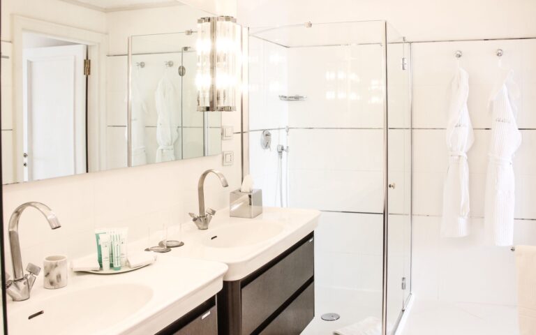 A suite bathroom with twin vanities, a walk-in shower and robes, Baglioni Resort Cala del Porto