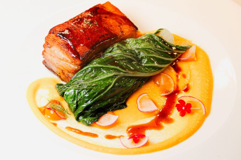 A plated main of fish with charred greens and a citrus sauce, Baglioni Resort Cala del Porto