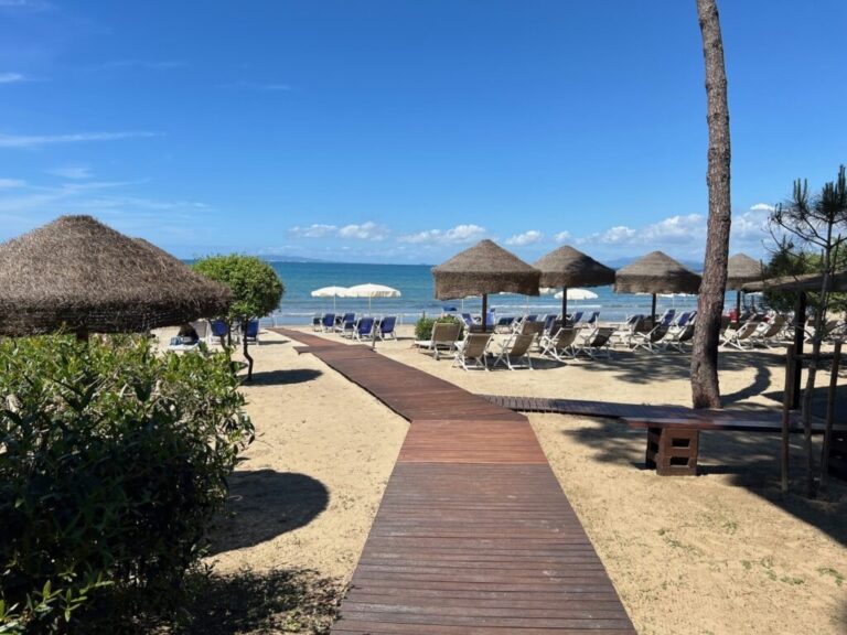 The boardwalk to the beach club, straw parasols and the sea beyond, Baglioni Resort Cala del Porto