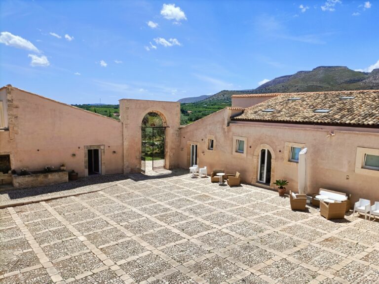Inner courtyard of the baglio with the arched gateway and mountains beyond, Ballium Luxury Relais